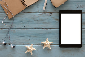 Top view of computer tablet, starfishes, headphones, note book. pen on a blue wooden background. Free space for text.