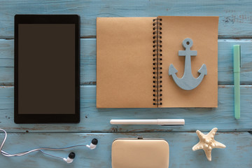 Travel concept with computer tablet, note book, anchor, star fish, pens, headphones on a blue wooden background. Free space for text.