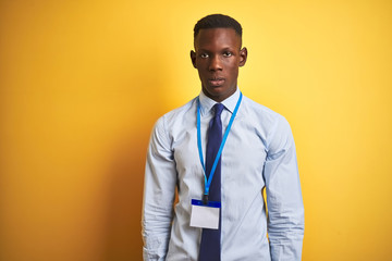 African american businessman wearing identification card over isolated yellow background with serious expression on face. Simple and natural looking at the camera.