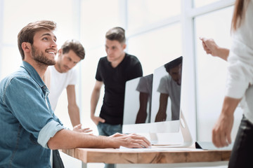 young man working on a computer sitting at the office table.