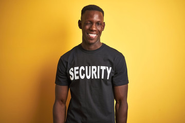 African american safeguard man wearing security uniform over isolated yellow background winking...