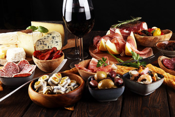 Italian antipasti wine snacks set. Cheese variety, Mediterranean olives, seafood salad, Prosciutto di Parma, tomatoes, anchovy and wine in glasses