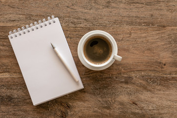 Top view of open notebook with blank pages and cup of coffee on a wooden background.