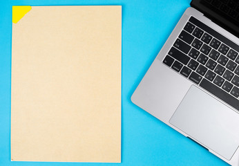 Laptop and brown paper sheet on a blue background.