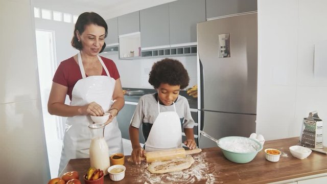 Young family cooking food in kitchen. Happy Little girl with her mother mixing batter. Mother and Little boy preparing the dough. Happy family in the kitchen and junior chef Concept. Cinematic 4k.