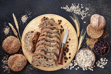 High fibre health food concept with raisin rye bread loaf, seeded rolls, raisins, muesli, seeds & sheaths of grain. High in antioxidants, omega 3, vitamins and protein with low gi. Flat lay, top view.