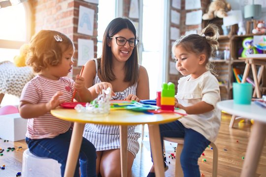 Young beautiful teacher and toddlers playing meals using plastic food and cutlery toy at kindergarten