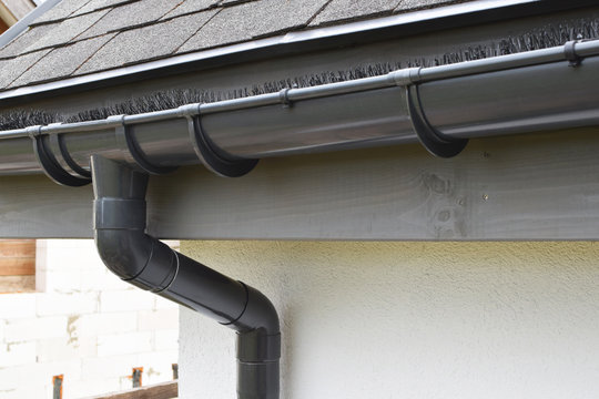 Plastic guard brush in new dark grey plastic rain gutter on asphalt shingles roof.