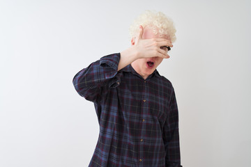 Young albino blond man wearing casual shirt and glasses over isolated white background peeking in shock covering face and eyes with hand, looking through fingers with embarrassed expression.