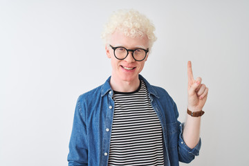 Young albino blond man wearing denim shirt and glasses over isolated white background showing and pointing up with finger number one while smiling confident and happy.