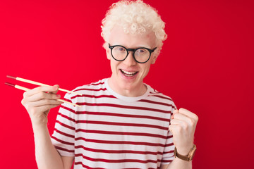 Young albino blond man holding chopsticks standing over isolated white background screaming proud and celebrating victory and success very excited, cheering emotion