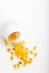 Top view of Gold fish oil scattered from pill bottle isolated for good health on white background. Supplementary food. Omega 3. Vitamin E. Capsules salmon fish oil