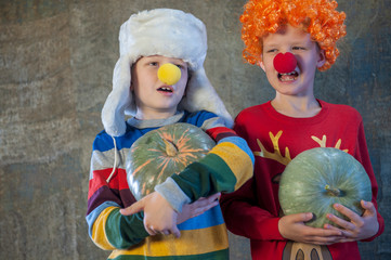 Two boys brothers in bright festive attire are holding pumpkins in their hands. Children dictate their message to Santa Claus before Christmas. Pupils sing songs and talk about successful studies