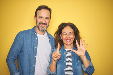 Beautiful middle age couple together wearing denim shirt over isolated yellow background showing and pointing up with fingers number six while smiling confident and happy.