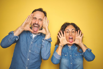 Beautiful middle age couple together standing over isolated yellow background Smiling cheerful playing peek a boo with hands showing face. Surprised and exited