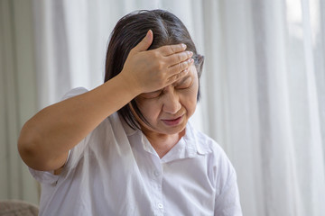 Asian senior woman sitting on sofa having headache at home. old female   stressed dizzy . elderly...