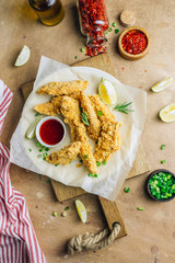 Breaded chicken strips with tomato sauces on a plate. Fast food on beige rustic background. Top view. Flat lay