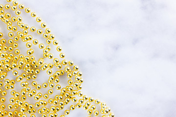 Golden christmas beads on marble background. Christmas frame. Line of golden beads garland on a white background. Top view. Copy space