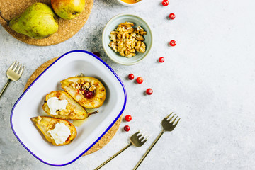 Sweet baked pears with honey, nuts, cranberries and cinnamon in enameled baking bowl on stone background. Top view. Flat lay