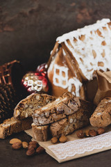 Christmas cookies and nuts.  Cantuccini (or biscotti) are crunchy Italian almond biscuits - with  a gingerbread house as background.