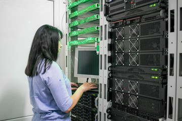 A female programmer is working in a server room. The girl is standing next to the computer racks of...