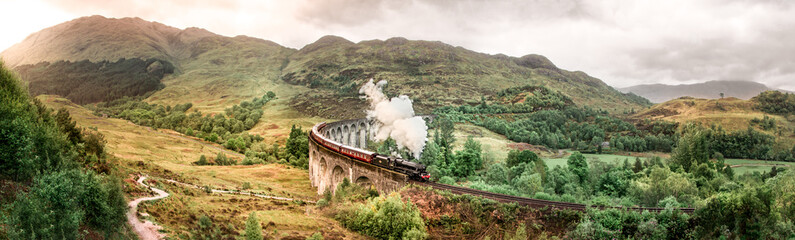 Glenfinnan-spoorwegviaduct met Jacobite-stoomtrein die overgaat. Harry Potter beroemde Glenfinnan viaduct, Schotland bij bewolkt weer met stoomtrein.