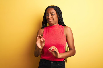 African american woman wearing red casual t-shirt standing over isolated yellow background disgusted expression, displeased and fearful doing disgust face because aversion reaction. With hands raised