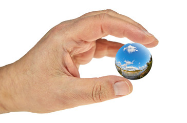 Eine Hand vor weißem Hintergrund greift eine Kugel mit einer Landschaft.