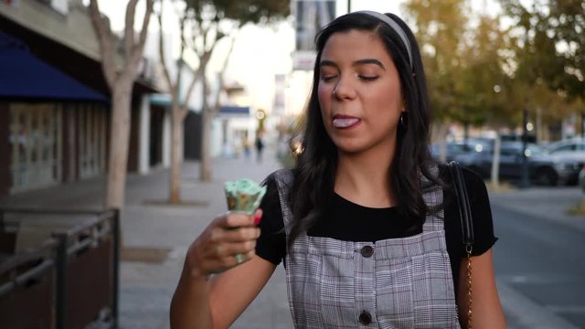 A cute young woman eating a messy ice cream cone dessert on a city street in slow motion.