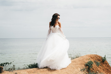 Beautiful bride in a white dress, in black glasses, stands on a rock