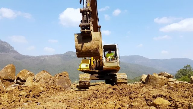 A construction worker driving a excavator with a large bucket on a mountain ridge moving closely towards the camera for a unique view
