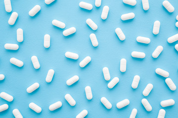 White pills on light pastel blue table. Drugs pattern. Medical, pharmacy and healthcare concept. Closeup. Top down view. - obrazy, fototapety, plakaty