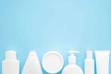 Different white toiletries on light pastel blue table. Care about face, hands, legs and body skin. Women beauty products. Empty place for text or logo. Flat lay. Top down view.