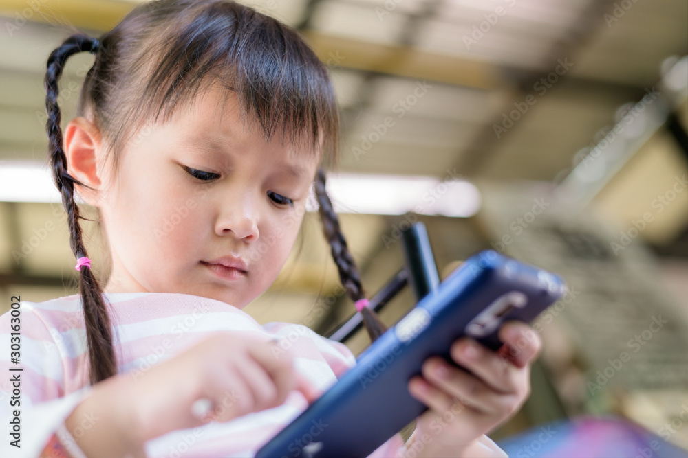 Aufkleber asian child little girl playing game or watching video on mobile phone. concept smartphone addiction