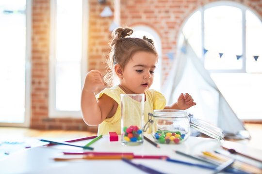 Beautiful toddler standing playing with chocolate colored balls on the table at kindergarten