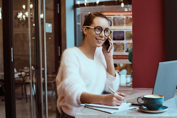 Woman entrepreneur working from cafe and talking on mobile phone with headphones