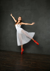 Fototapeta na wymiar girl in a white translucent dress in red pointes on a gray background