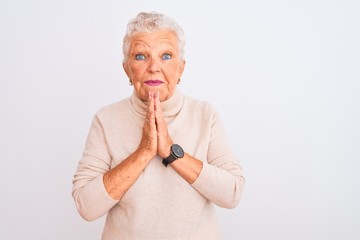 Senior grey-haired woman wearing turtleneck sweater standing over isolated white background praying with hands together asking for forgiveness smiling confident.