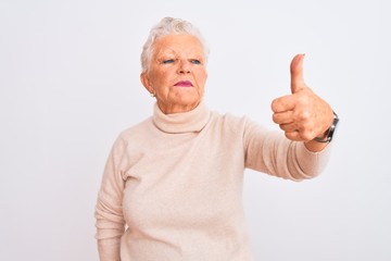 Senior grey-haired woman wearing turtleneck sweater standing over isolated white background Looking proud, smiling doing thumbs up gesture to the side