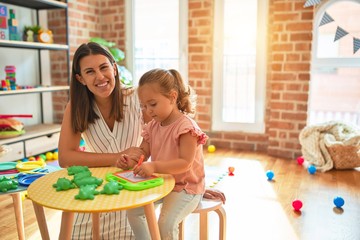 Beautiful teacher and blond student toddler girl drawing using digital board at kindergarten