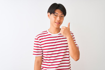 Young chinese man wearing glasses and striped t-shirt standing over isolated white background doing happy thumbs up gesture with hand. Approving expression looking at the camera showing success.