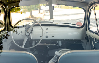 Interior of small white vintage car on the street. No people. White steering wheel.