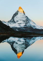 Alpenglow on Matterhorn during sunrise, reflected in lake Riffelsee. Alpine mountains in...