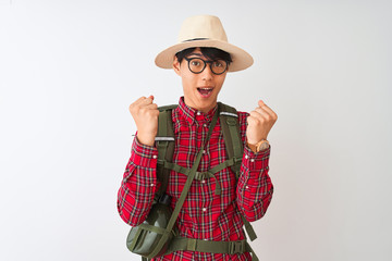 Chinese hiker man wearing backpack canteen glasses hat over isolated white background celebrating surprised and amazed for success with arms raised and open eyes. Winner concept.