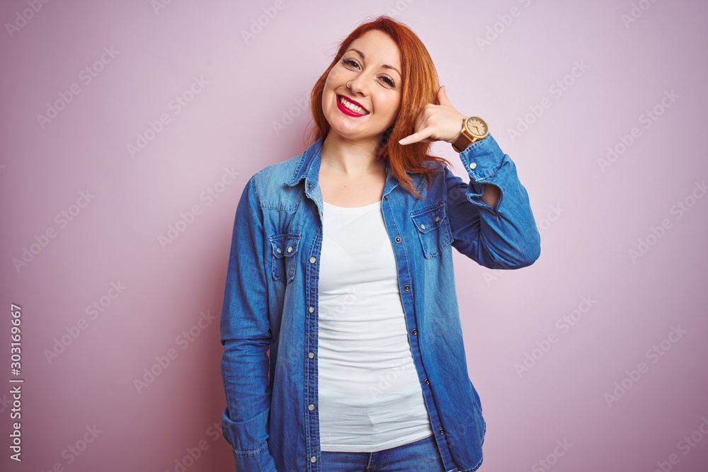 Sticker Youg beautiful redhead woman wearing denim shirt standing over isolated pink background smiling doing phone gesture with hand and fingers like talking on the telephone. Communicating concepts.