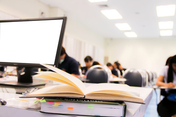 A notebook/pen/books/grasses of teacher on table and students during study or quiz, test and exam in large lecture room / University classroom. Students are in uniform classroom educational school.