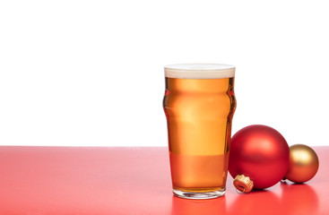 Pint glass of ale or beer with christmas baubles on red background