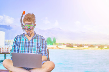 A man in an underwater mask, on vacation at sea, working at a computer.