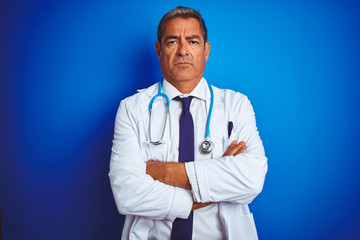 Handsome middle age doctor man wearing stethoscope over isolated blue background skeptic and nervous, disapproving expression on face with crossed arms. Negative person.
