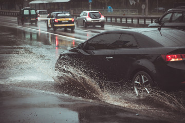 Ukraine. Kiev - 05,12,2019 Spraying water from the wheels of a vehicle moving on a wet city asphalt road. The wet wheel of a car moves at a speed along a puddle on a flooded city road during rain.